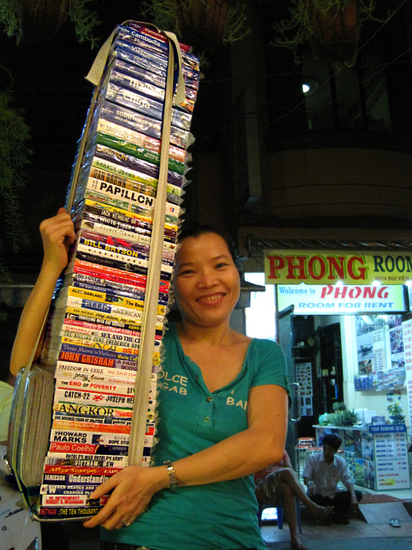 Woman in Ho Chi Minh City (Saigon) with a stack of counterfeit books for sale