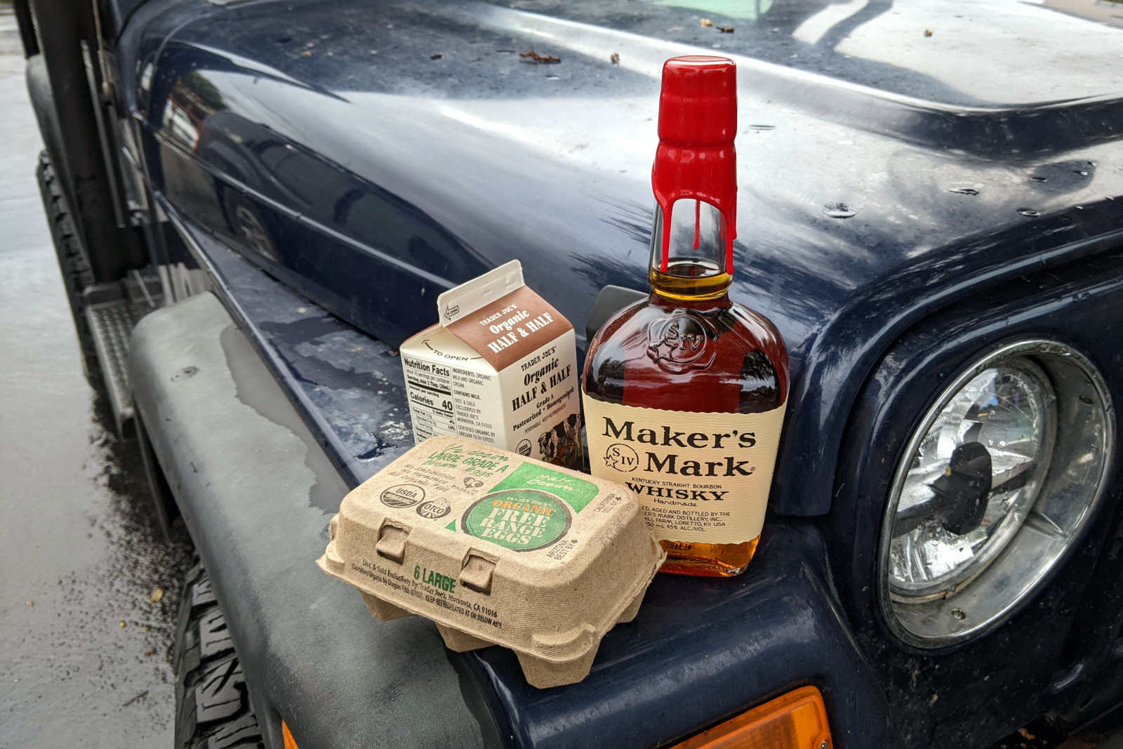Ingredients for a batch of aged eggnog (Maker's Mark bourbon, half-and-half, eggs) sitting on Jeep fender