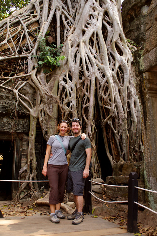 Stephanie and Justin posing on the platform in front of the strangler fig growing on Ta Prohm in Angkor, Cambodia