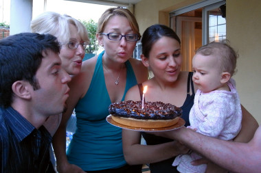 Justin, Chris, Stephanie, and Aurelie help Luna blow out the candle on her first birthday cake