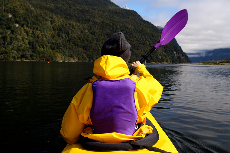 View of Stephanie's back in a tandem kayak while paddling Milford Sound